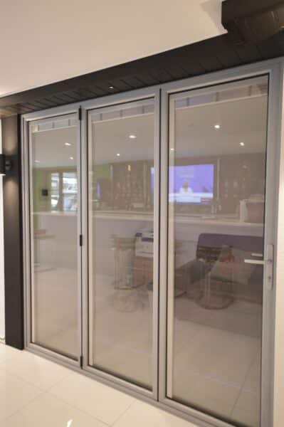picture of light grey bifold doors with integral blinds in a glazing showroom